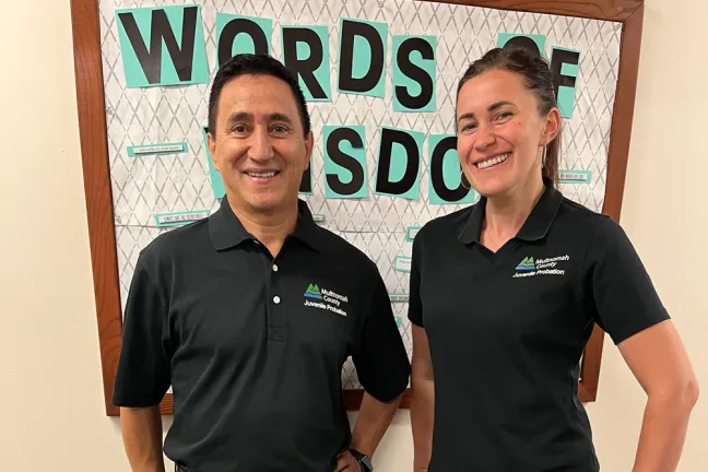 Two juvenlie court counselors pose in front of a bulletin board that says "Words of Wisdom"