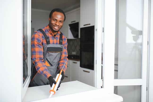 A person caulks a window and looks at the camera with a smile