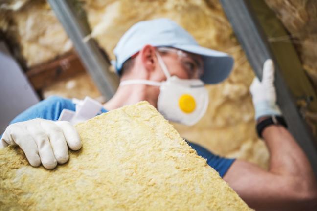 A person wearing a respirator installs insulation in a wall