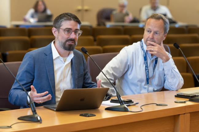 Ryan Deibert and Dan Feild sit at dais in board room.