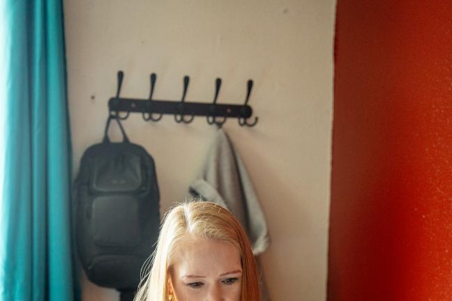 Wendie Smith sits behind a computer in a room with a red wall