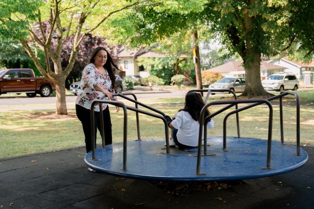 A woman spins a child around on a playground merry-go-round.