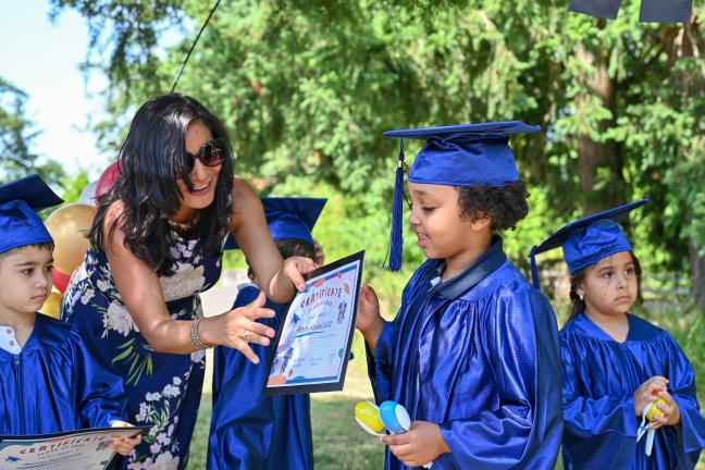 A teacher hands a preschooler an award at IRCO's preschool graduation.