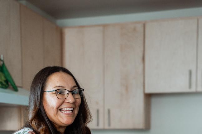 A woman smiles standing in her kitchen.