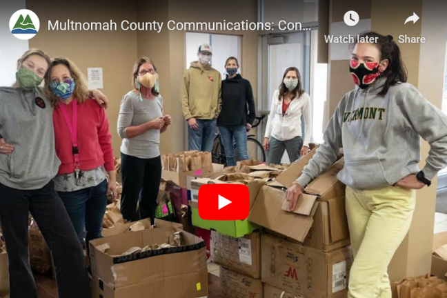 A group of people working together pose in front of a big delivery of face masks