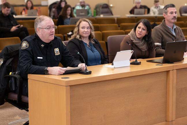 A panel of four invited guests sitting at a brown podium in the foreground with guests seated in the background.