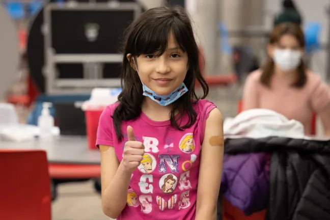 Girl in a pink shirt gives a thumbs up after receiving vaccines.