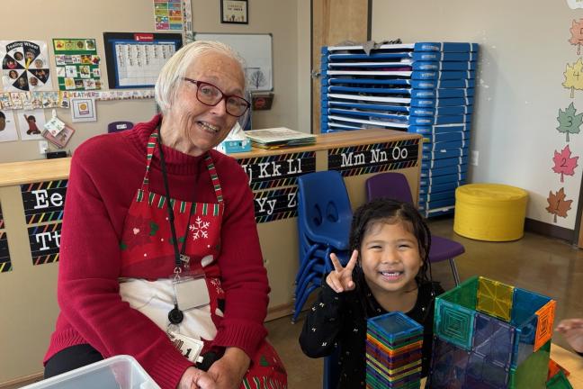 Foster grandparent sits with young preschool. 