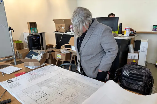 Commissioner Meghan Moyer is reading large blueprint page opened on a work desk at Central City Concerns Burnside Recovery Center.