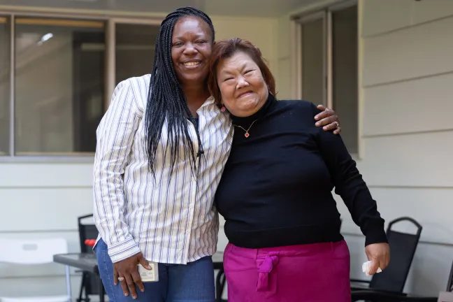 Two women smiling and embracing outdoors.