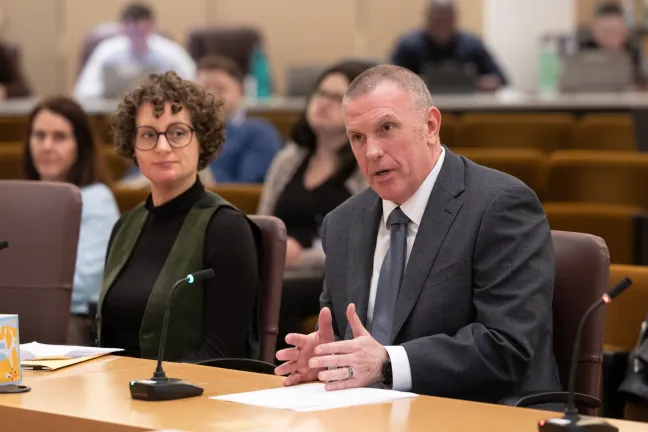 Elections Director Tim Scott and Leah Benson, the County’s ranked-choice voting project manager are sitting at a conference table with microphones -- presenting before the Multnomah County Board.