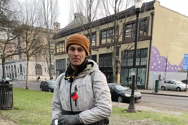 Person dressed in cold weather clothes standing behind his bike in the North Park Blocks of downtown Portland.