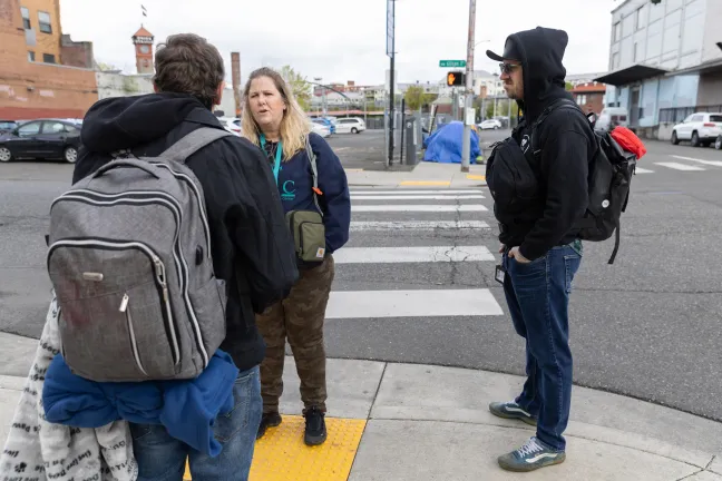 Two MHAAO staff members face and talk with an unidentified individual wearing a backpack and carrying a blanket, whose back is facing the camera