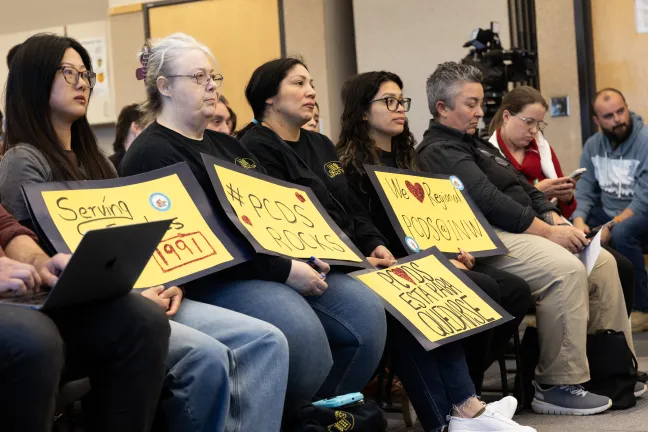 Community members sitting holding yellow signs up in support of the PCDS program