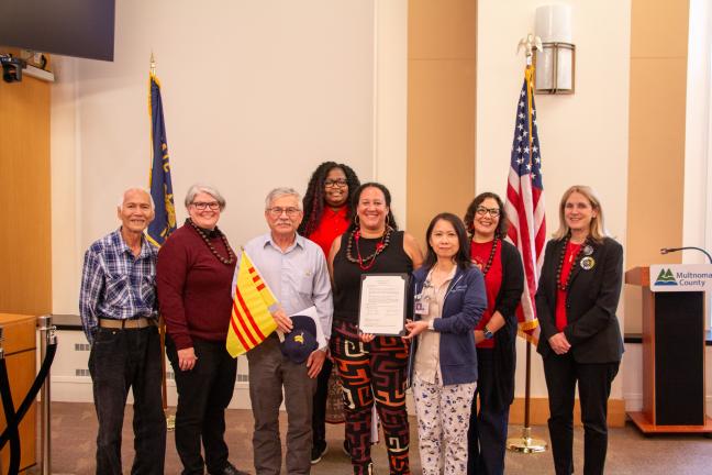 Board of County Commissioners and community members pose for photo, holding Vietnam flags.