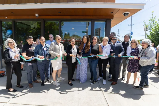 A large group of County and community leaders cut a blue ribbon in front of a new Community Health Center.