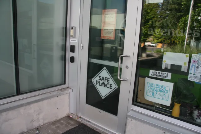 An angled, eye-level shot of the glass entrance door to a building. On the door is a prominent, black-and-white diamond-shaped sign that reads "SAFE PLACE".