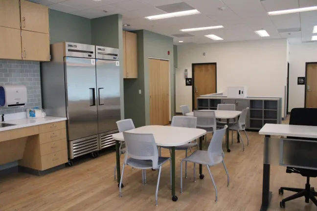 A room with a refrigerator, tables and chairs.