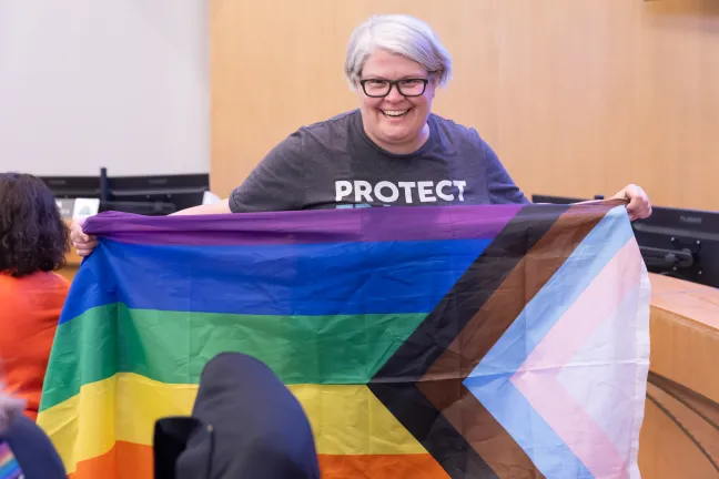 Commissioner Meghan Moyer smiles and holds up a Pride flag.