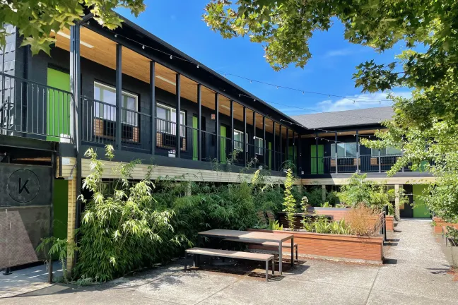 Exterior of a motel painted black with green doors and an outdoor patio.