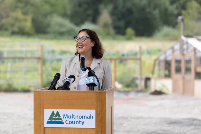 Chair Jessica Vega Pederson is speaking outside of a farm behind a podium labeled "Multnomah County"