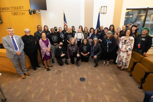 County staff and community members stand with the Board of County Commissioners in a boardroom with the signed proclamation. 