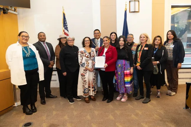 County staff and community members stand with the Board of County Commissioners in a boardroom with the signed proclamation. 