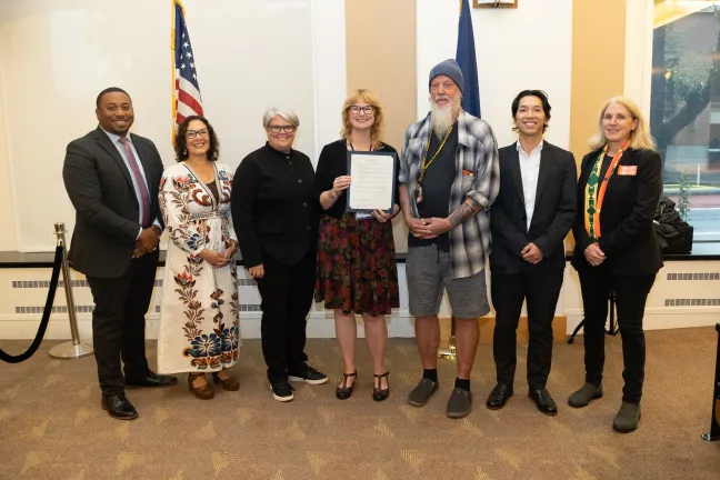 County staff stand with the Board of County Commissioners in a boardroom with the signed proclamation. 