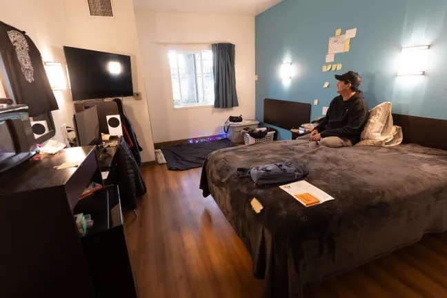 Wes sits in a tidy motel room.