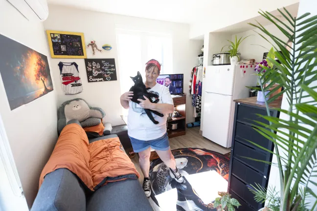 Cori stands in her apartment holding a black kitten.