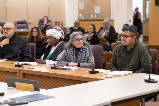 Four people sit behind a dais in the boardroom.