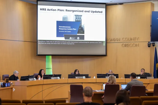 The Multnomah County Board of Commissioners sits at the dais with a presentation on the Homelessness Response System displayed behind them.