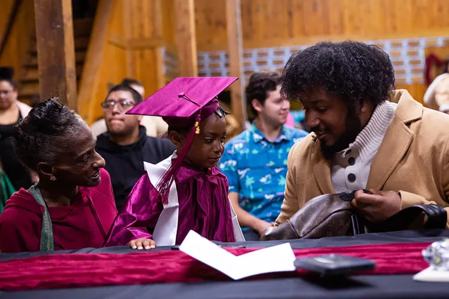 Two family members sit closely with a child at a preschool graduation