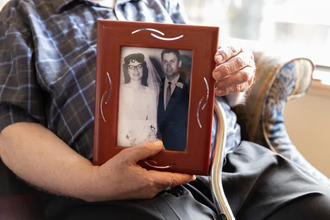 Man holds framed wedding photo of him and his wife. 
