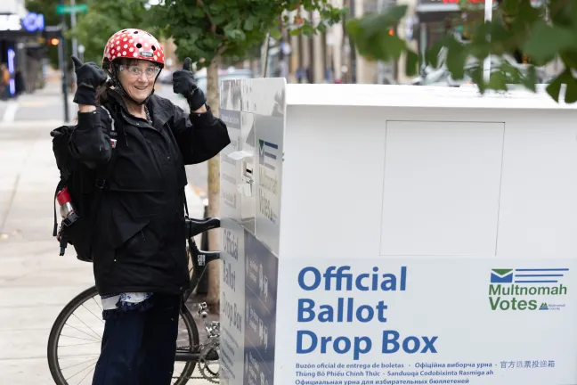 A voter on a bicycle drops off a ballot at an Official Ballot Drop Box site. 