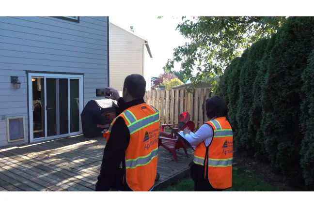 two appraisers wearing orange vests taking pictures of a new deck in a back yard. 