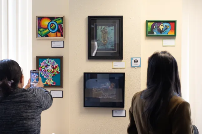 La gente toma fotos de las obras de arte en la Exposición de Arte sobre Discapacidades Intelectuales y del Desarrollo de 2025.
