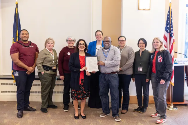 Board members, County staff and invited guests pose with the signed Mental Health Awareness Month proclamation in the boardroom.