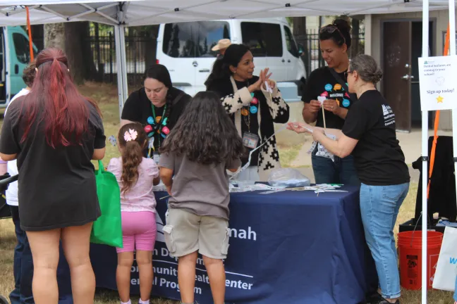 Representantes del Departamento de Salud del Condado de Multnomah reparten pegatinas a dos niños frente a un puesto. 