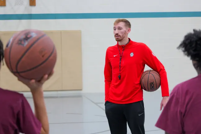 Basketball coach volunteer holding basketball with two youth one holding a basketball with backs to camera