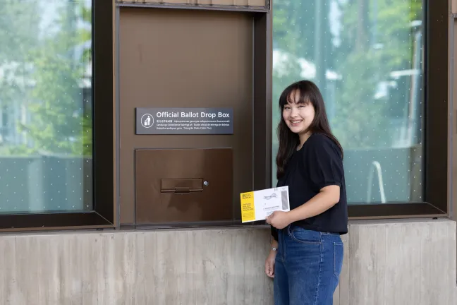 A voter holds a ballot return envelope next to an Official Multnomah County Ballot Drop Site at the East County Library. 