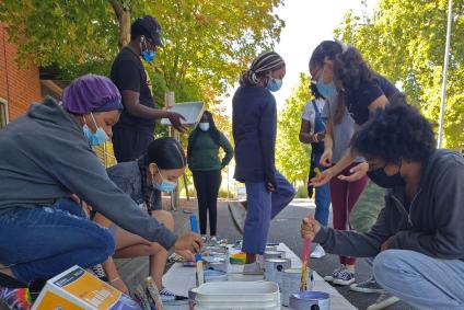 youth of color gather around a tarp to mix paint for a street mural