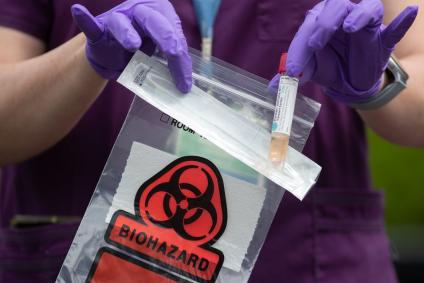 close up of a health worker in purple scrubs dropping a specimen vial into a red biohazard bag