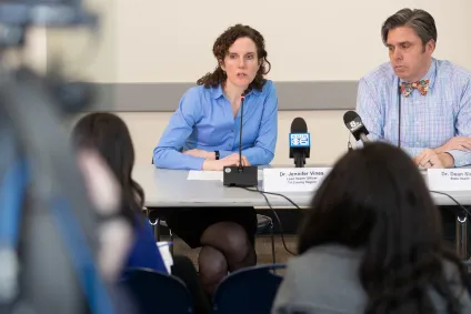 County and state health officers seated behind a table, talking to news media