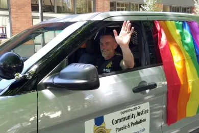 A DCJ staff member waves while driving a DCJ vehicle in the 2016 Pride Parade.