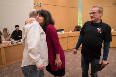 Commissioner Sharon Meieran hugs long-term survivor Terrance Gravening as Steven Headington looks on