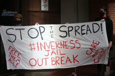 Photo of banner at MCSO protest that says, "Stop the spread - #Invernessjailoutbreak"