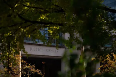 View of the entrance of the Multnomah County Detention Center through the tree branches across the street. Above the entrance an engraving that says in capital letters, "Justice Center".