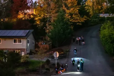 Masked trick or treaters (a group of kids accompanied by adults) walk down a hilly neighborhood street at dusk in Northeast Portland, Oct. 31, 2020.