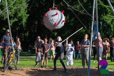 Kids whack away at a piñata shaped lie a COVID-19 virus. 